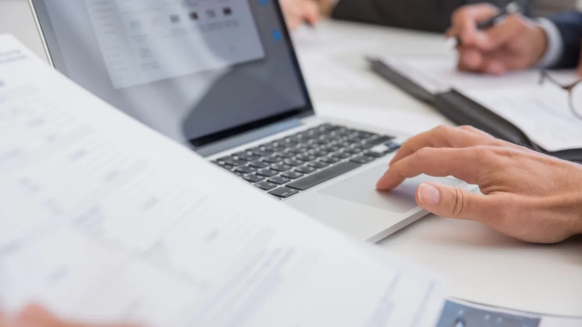 Business documents sit beside a laptop being used to configure a knowledge-based assistant (Photo by Kampus Production, Pexels)